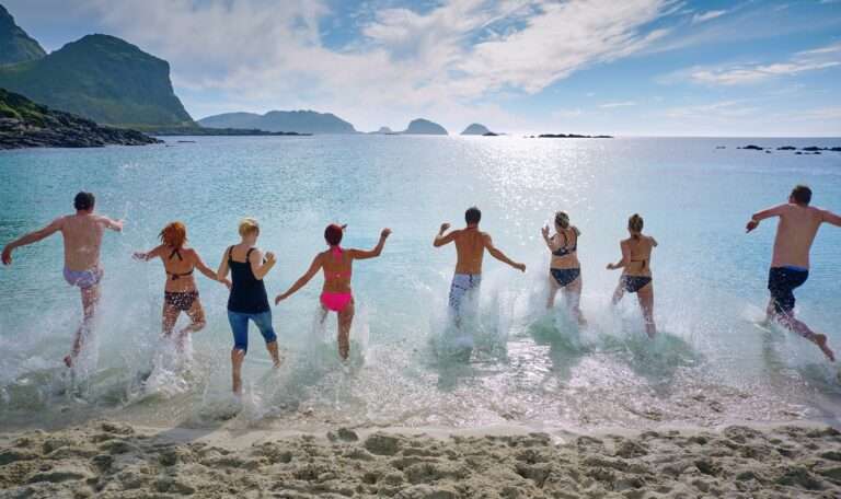 A line up of people run into the sea on holiday, the sun beams down and it is beautiful