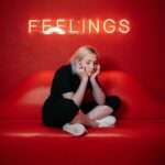 A woman on a red background sits on a chair with the word "Feelings" above her for an article on Houghton & Mackay