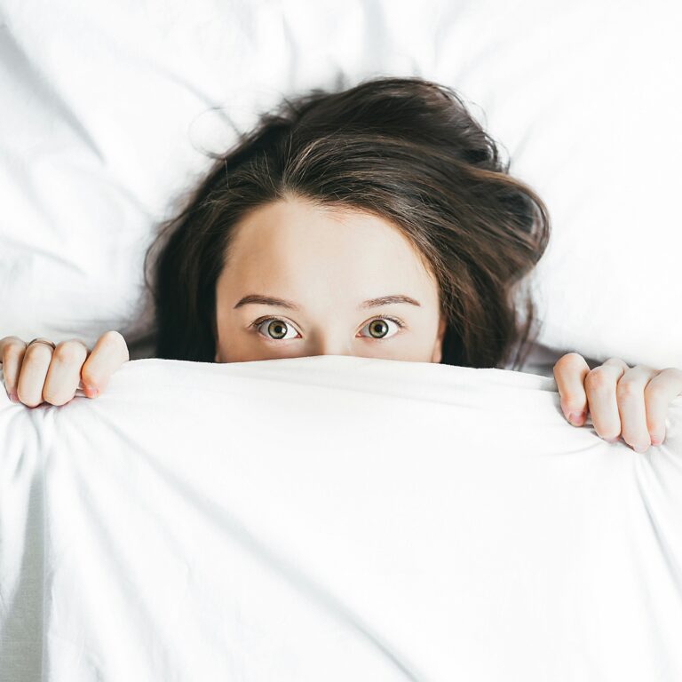 A lady hides under a blanket, staring at the camera for an article by Emily James for Houghton and Mackay Magazine