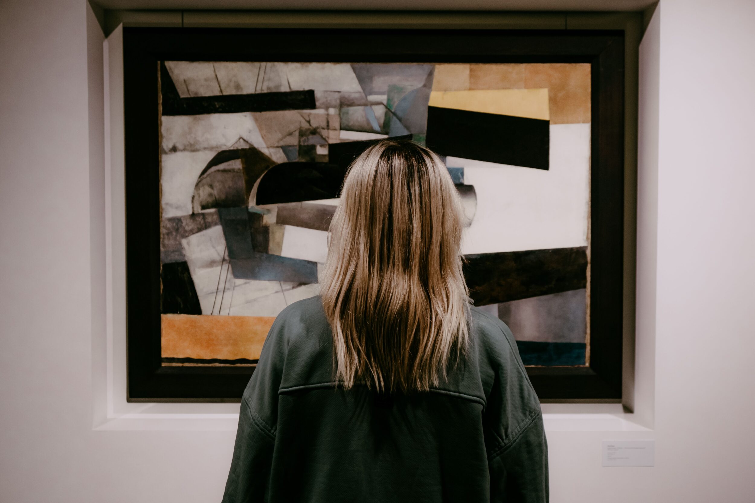 A woman stands in front of some art in a gallery, it is abstract.