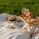 A picnic blanket is laid out with upper glass fayre.