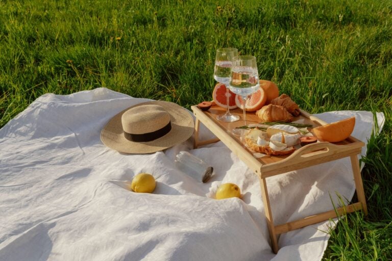 A picnic blanket is laid out with upper glass fayre.